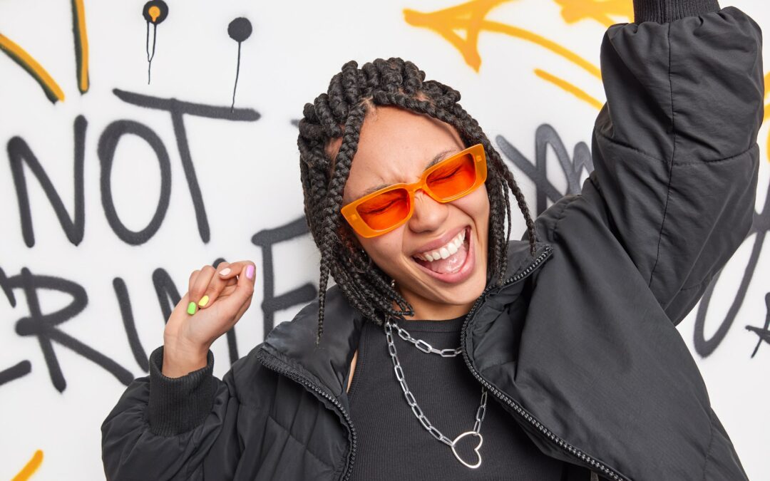 Hipster teen girl dances to pop music raises arms has fun sings song wears trendy orange sunglasses