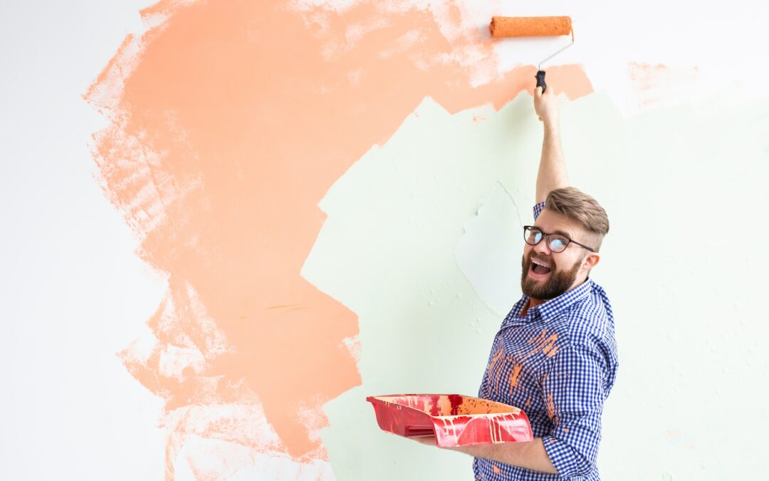 Male painting the wall with paint roller. Portrait of a funny guy painting wall in her new apartment